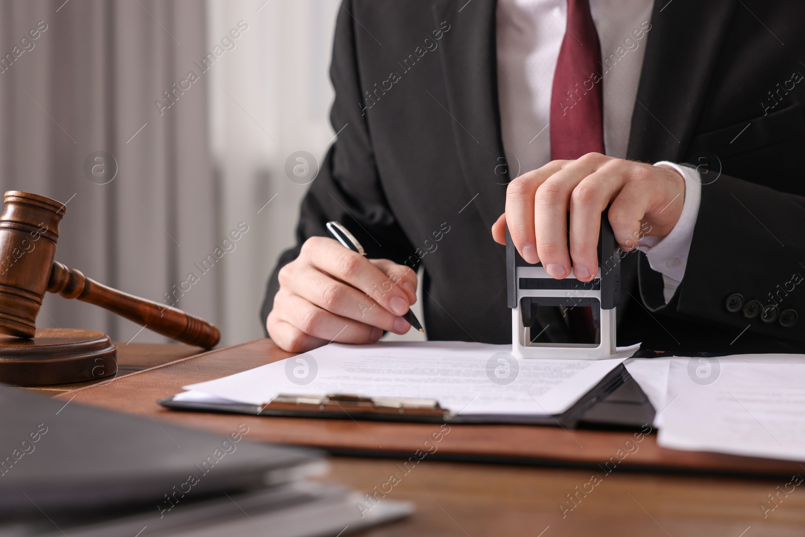 Photo of Notary with pen stamping document at wooden table in office, closeup