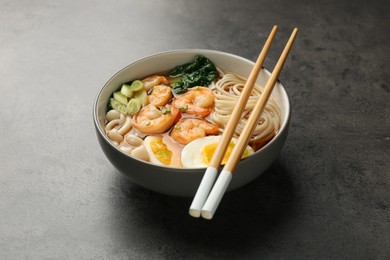 Photo of Delicious ramen with shrimps and chopsticks on grey table. Noodle soup