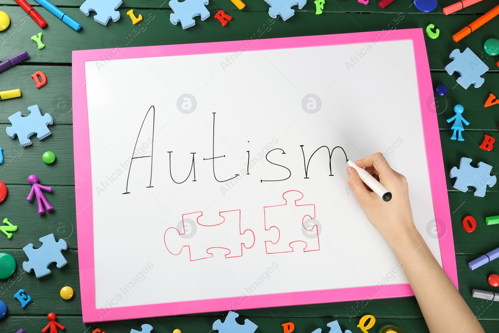 Photo of MYKOLAIV, UKRAINE - DECEMBER 30, 2021: Woman writing word Autism on white board at green wooden table with toys, top view