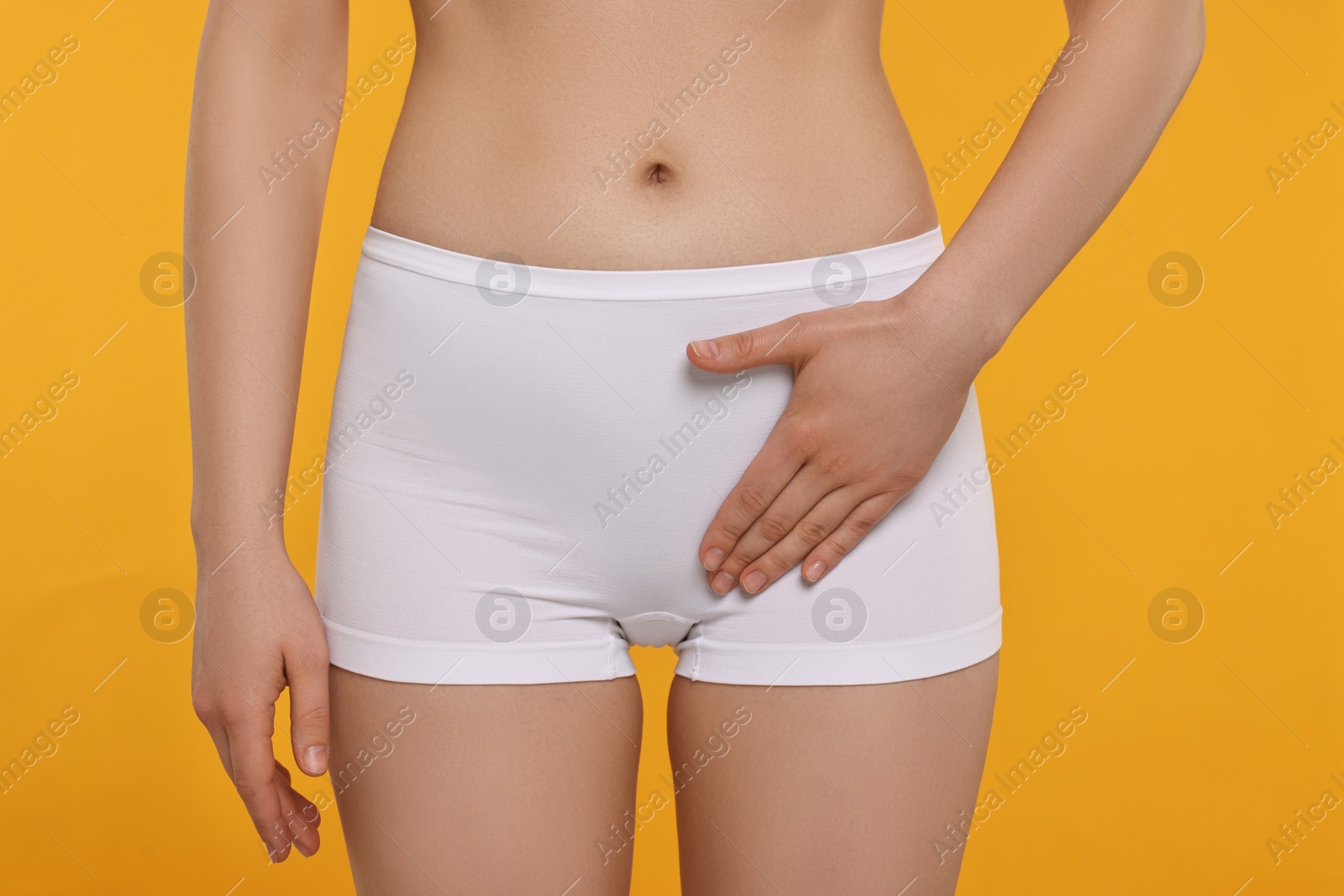 Photo of Woman holding hand near panties on orange background, closeup. Women's health