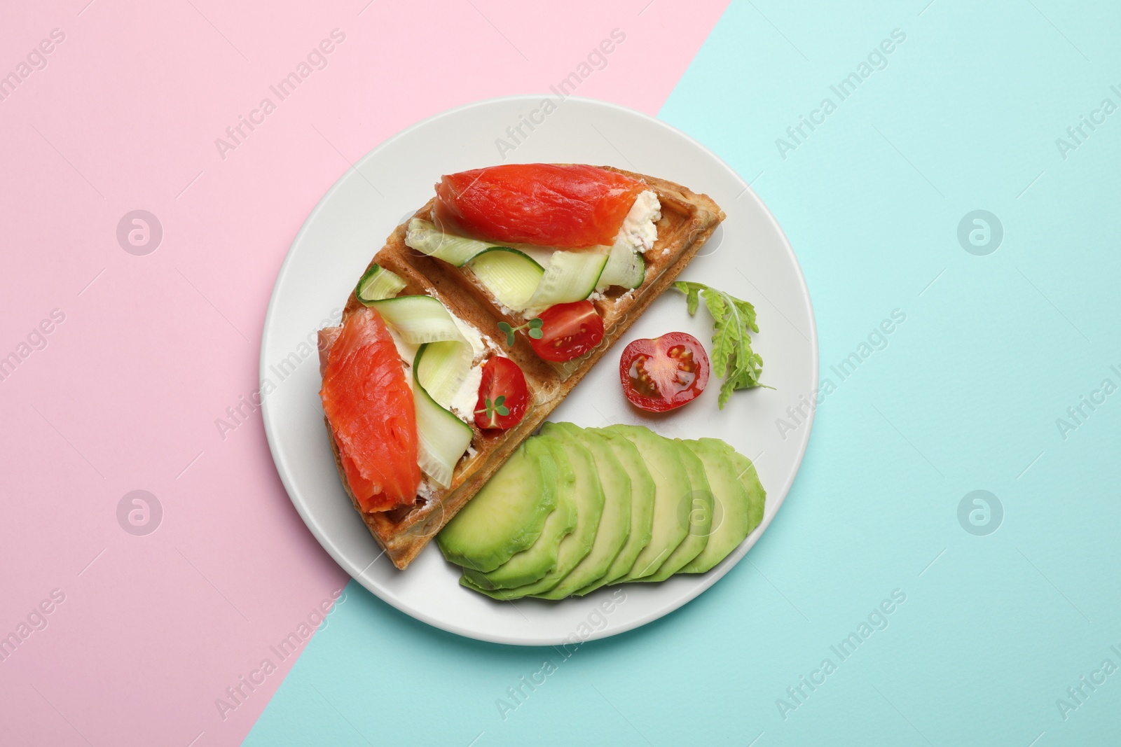 Photo of Delicious Belgian waffle with salmon, avocado, cream cheese and vegetables on color background, top view