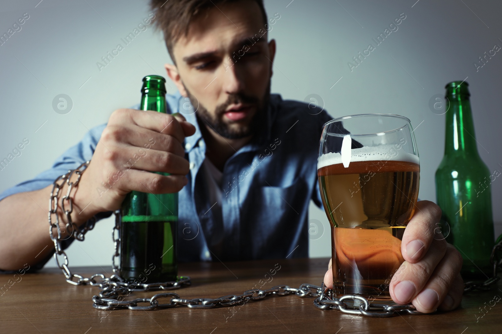 Photo of Addicted man chained to glass of alcoholic drink at wooden table, focus on hands