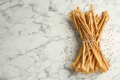 Photo of Delicious grissini sticks on white marble table, flat lay. Space for text