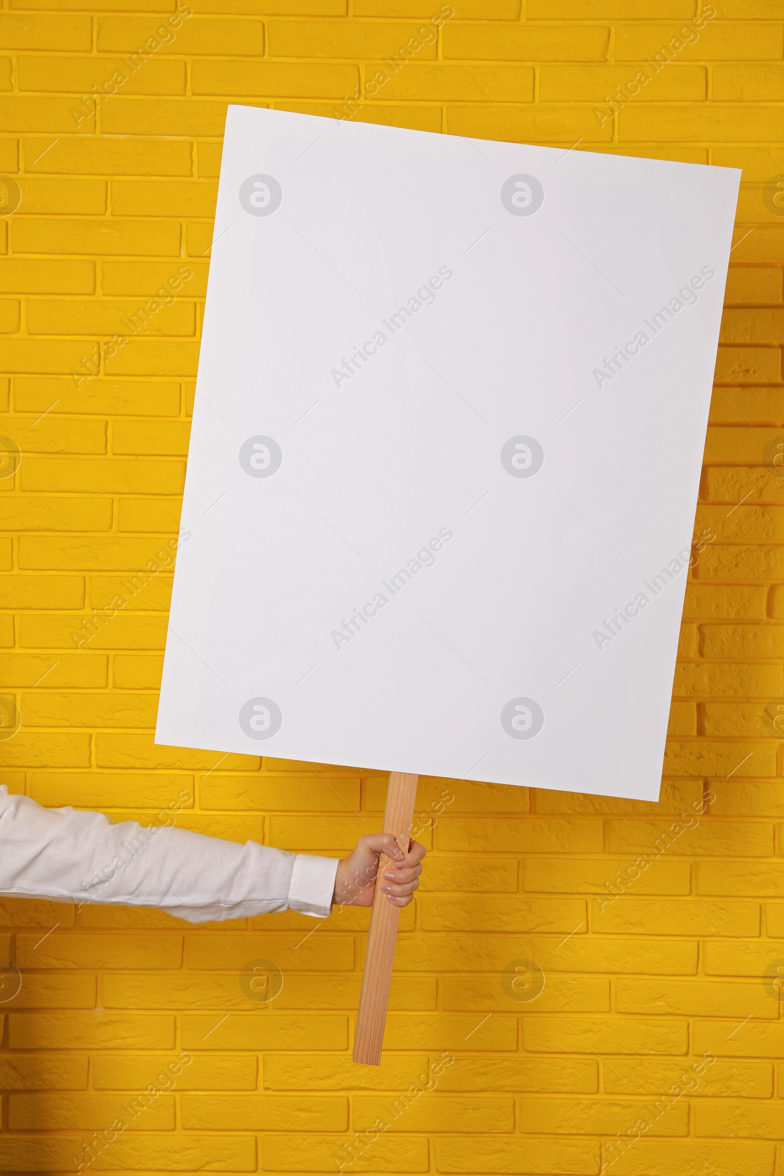 Photo of Woman holding blank sign near yellow brick wall, closeup. Space for design