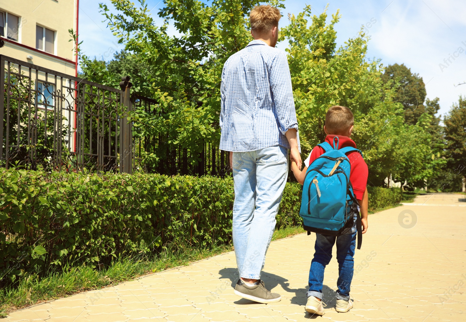 Photo of Young father taking his little child to school through park