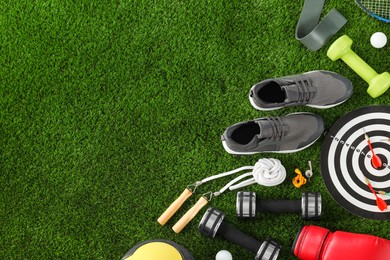 Photo of Different sport equipment and sneakers on green grass, flat lay. Space for text