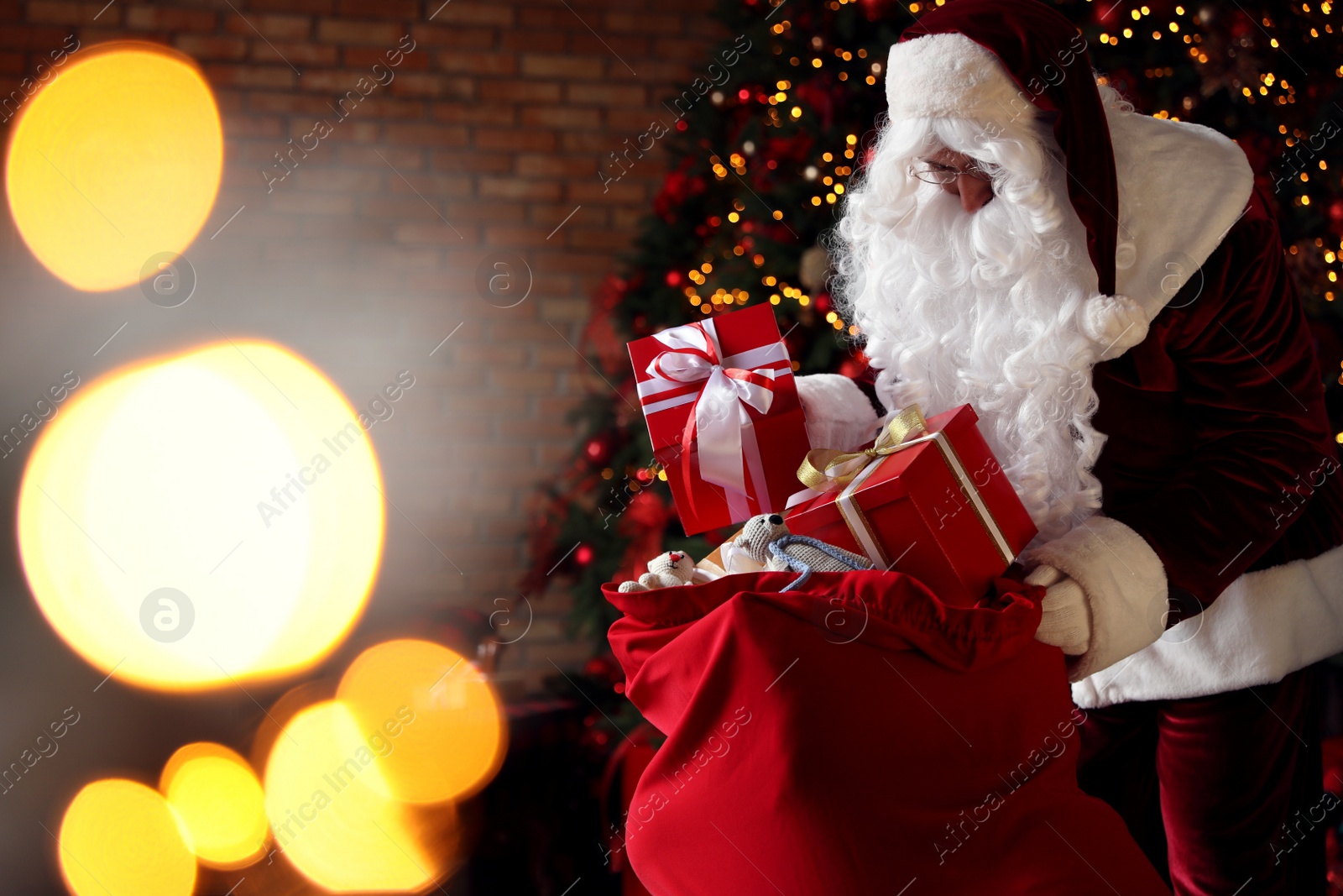 Photo of Santa Claus packing gifts into bag near Christmas tree