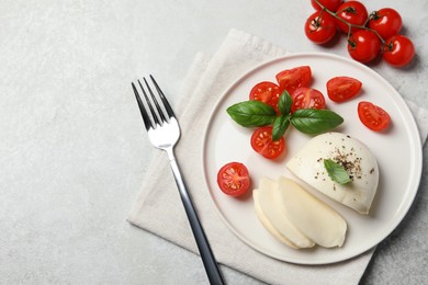 Delicious mozzarella with tomatoes, basil leaves and fork on light gray table, flat lay. Space for text