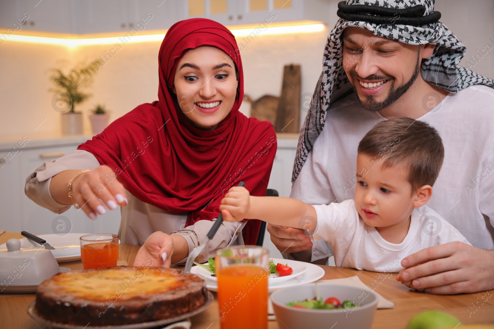 Photo of Happy Muslim family eating together at table in kitchen