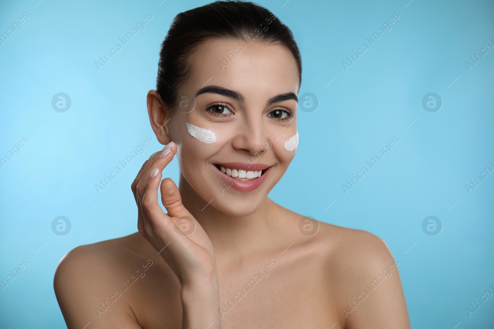 Photo of Young woman applying facial cream on light blue background