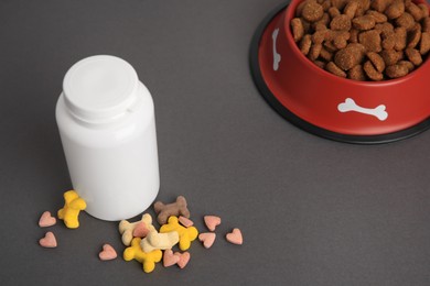 Bottle with vitamins and dry pet food in bowl on grey background, above view