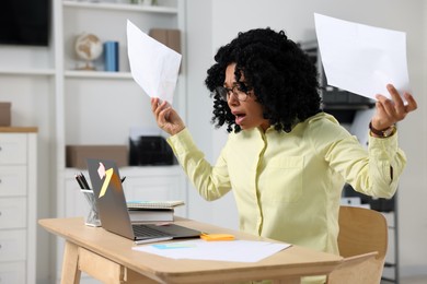 Deadline concept. Scared woman holding documents and looking at laptop in office