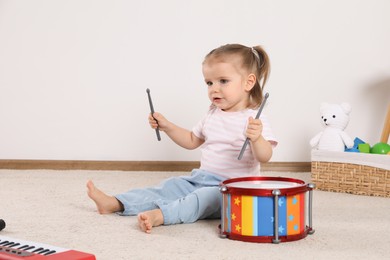 Photo of Cute little girl playing with drum and drumsticks at home