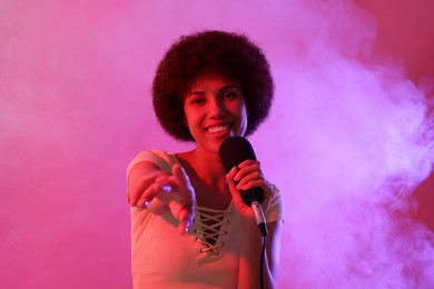 Curly young woman with microphone singing on pink background. Color tone effect