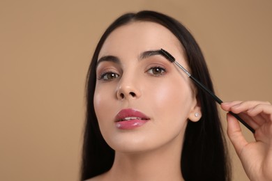 Woman applying makeup with eyebrow brush on light brown background