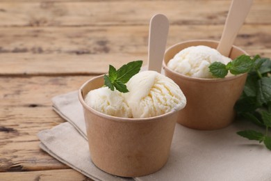 Photo of Paper cups with delicious ice cream and mint on wooden table, closeup