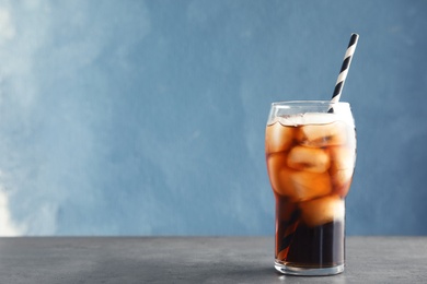 Photo of Glass of refreshing cola with ice on table against color background. Space for text