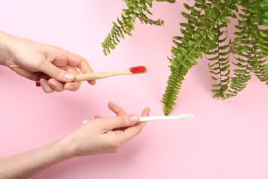 Photo of Woman holding natural bamboo and plastic toothbrushes on pink background, top view