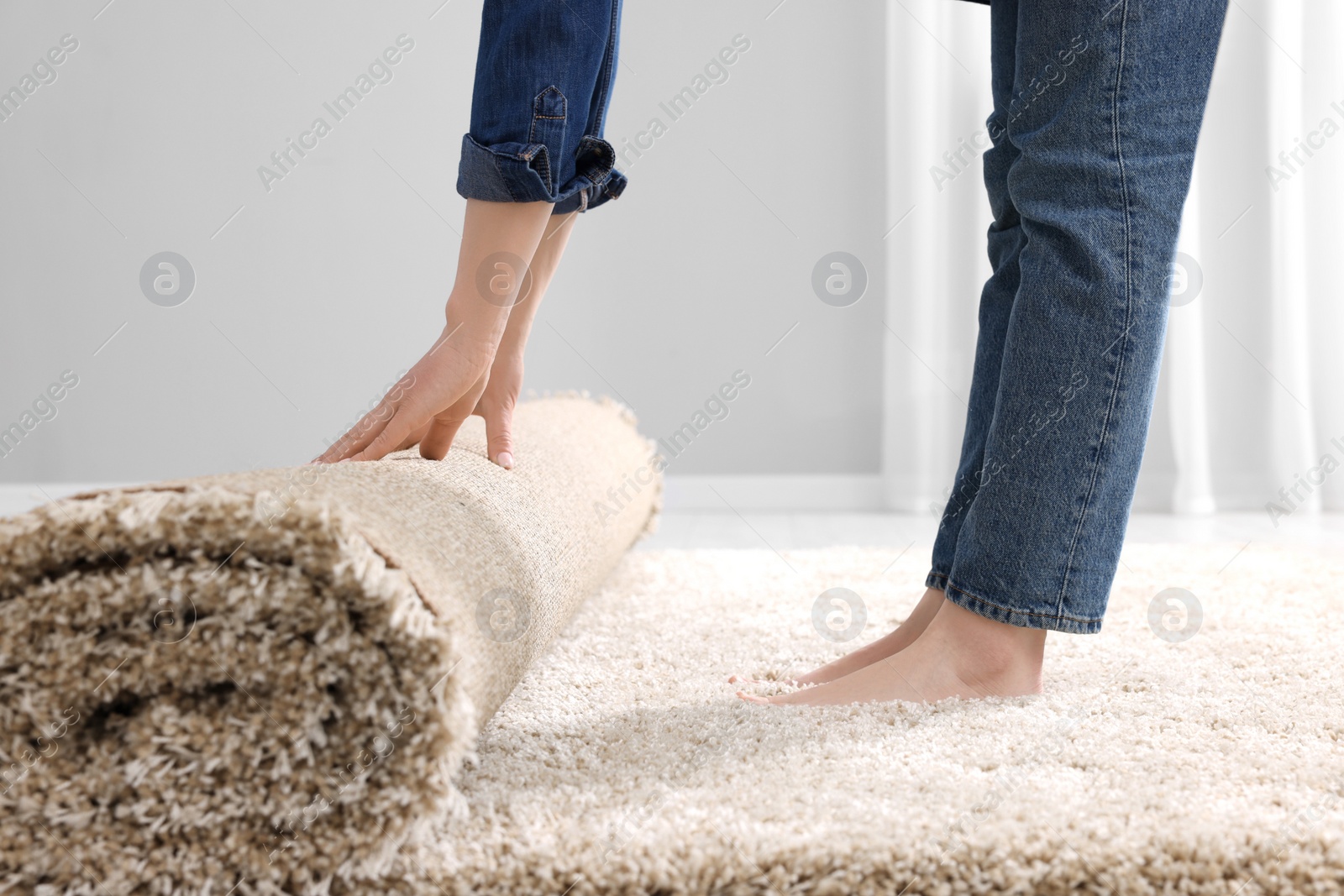 Photo of Woman unrolling carpet on floor in room, closeup