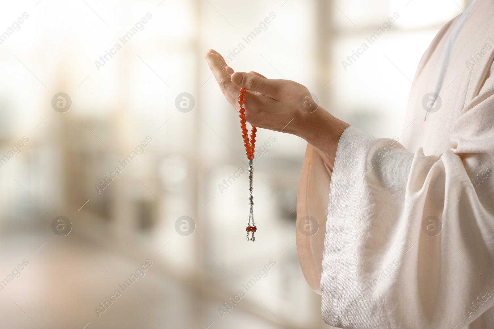 Image of Muslim man with misbaha praying on blurred background, closeup. Space for text