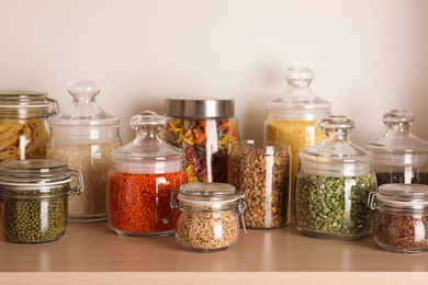 Glass jars with different types of groats on wooden shelf