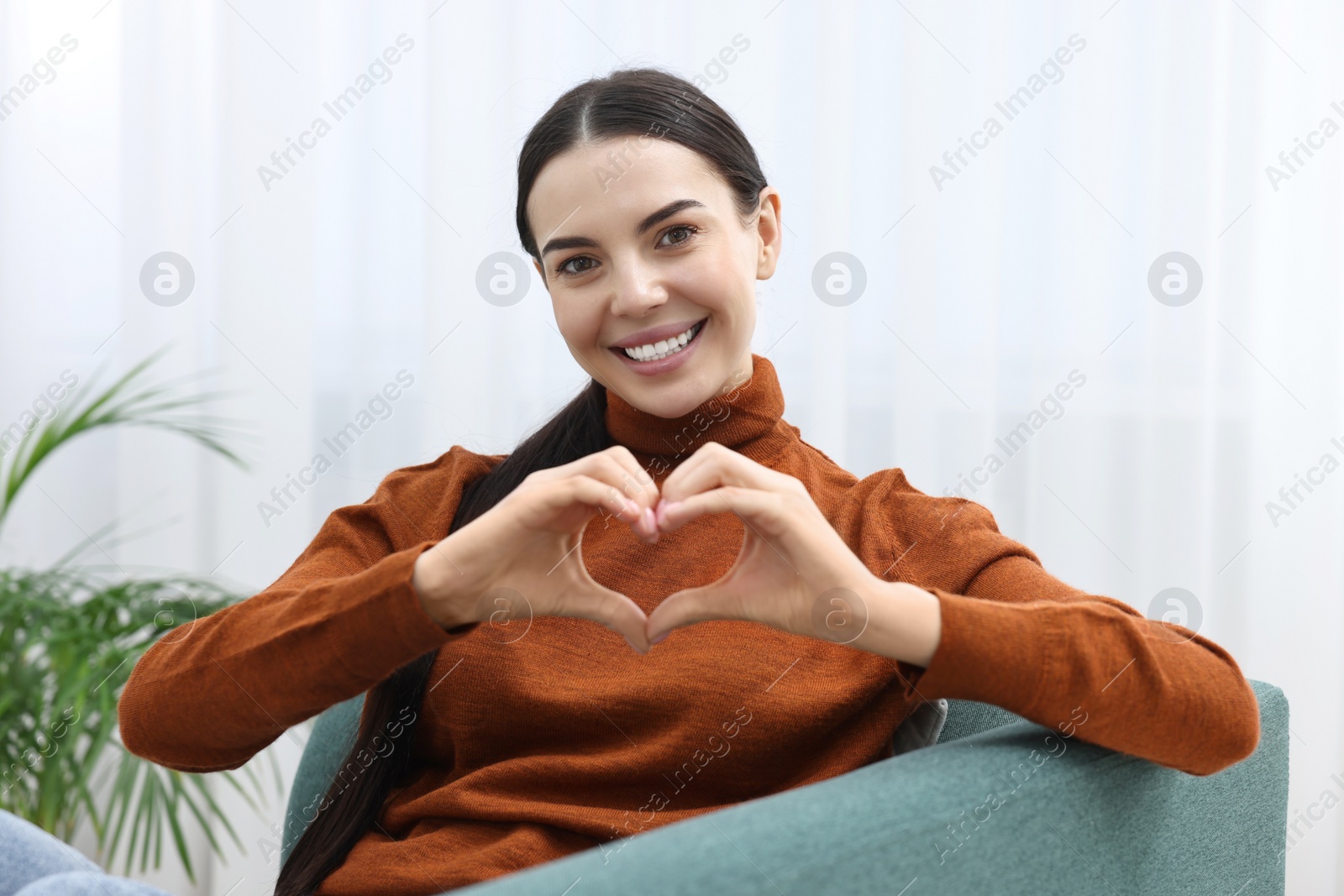 Photo of Happy young woman making heart with hands at home