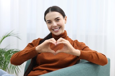 Happy young woman making heart with hands at home