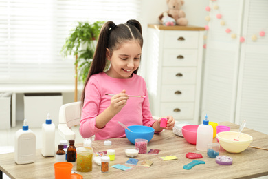 Photo of Cute little girl making homemade slime toy at table indoors