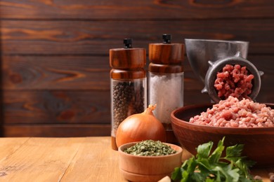 Photo of Manual meat grinder with beef mince, spices and parsley on wooden table, space for text