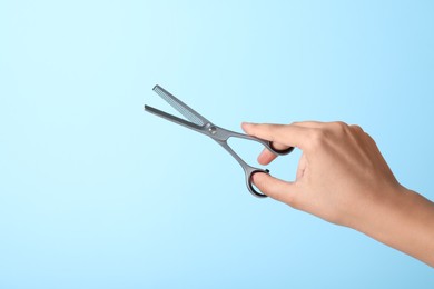 Photo of Hairdresser holding professional thinning scissors on turquoise background, closeup. Haircut tool