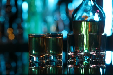 Photo of Drink alcohol in shot glasses and bottle on mirror surface against blurred background, closeup
