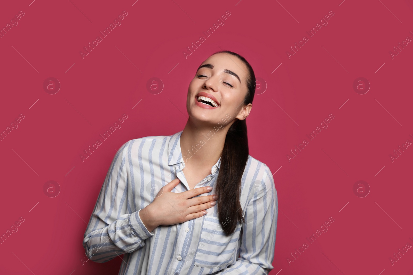 Photo of Beautiful young woman laughing on maroon background. Funny joke