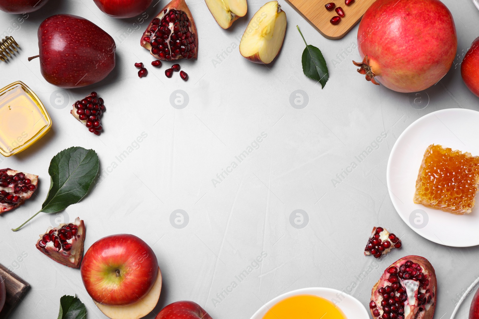 Photo of Frame of honey, apples and pomegranates on light table, flat lay with space for text. Rosh Hashanah holiday