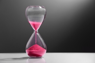Photo of Hourglass with pink flowing sand on color background. Space for text