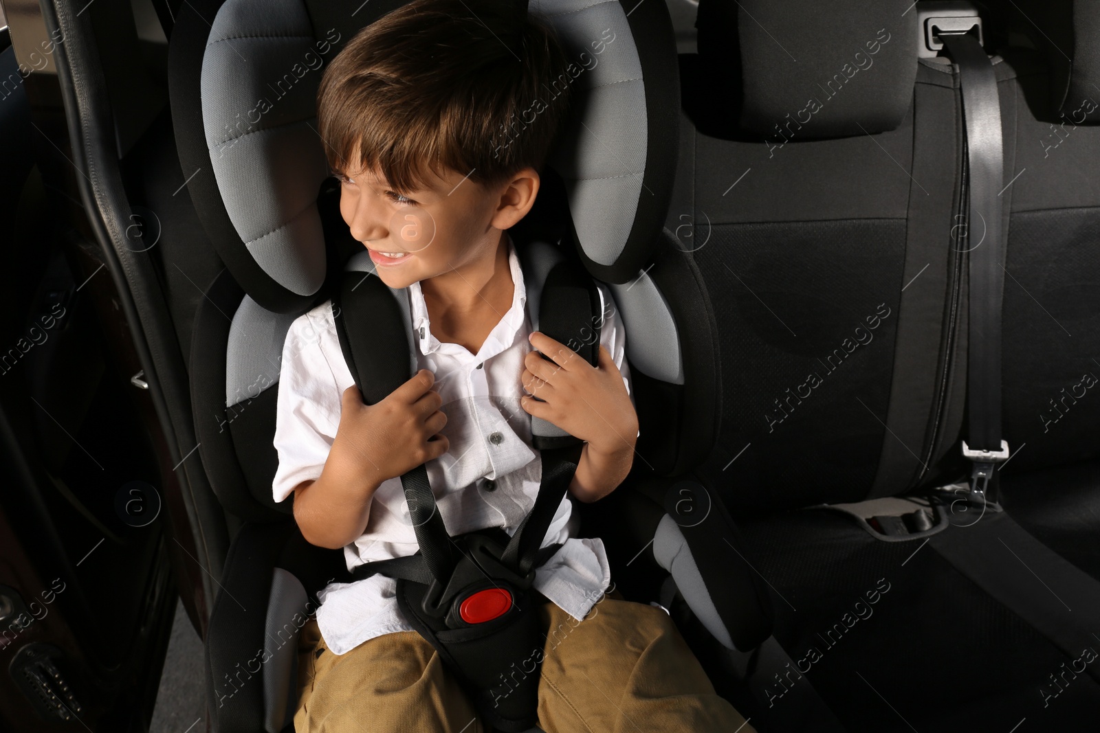 Photo of Little boy fastened with car safety belt in child seat