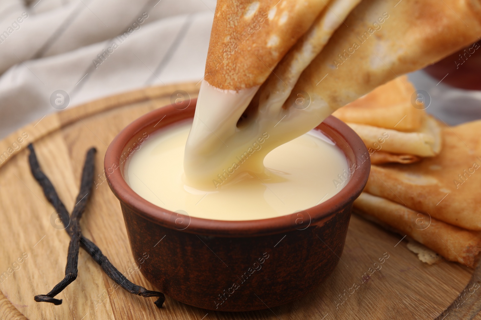 Photo of Dipping crepe into tasty condensed milk at table, closeup