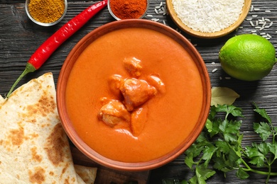 Photo of Delicious butter chicken served on wooden table, flat lay. Traditional indian Murgh Makhani