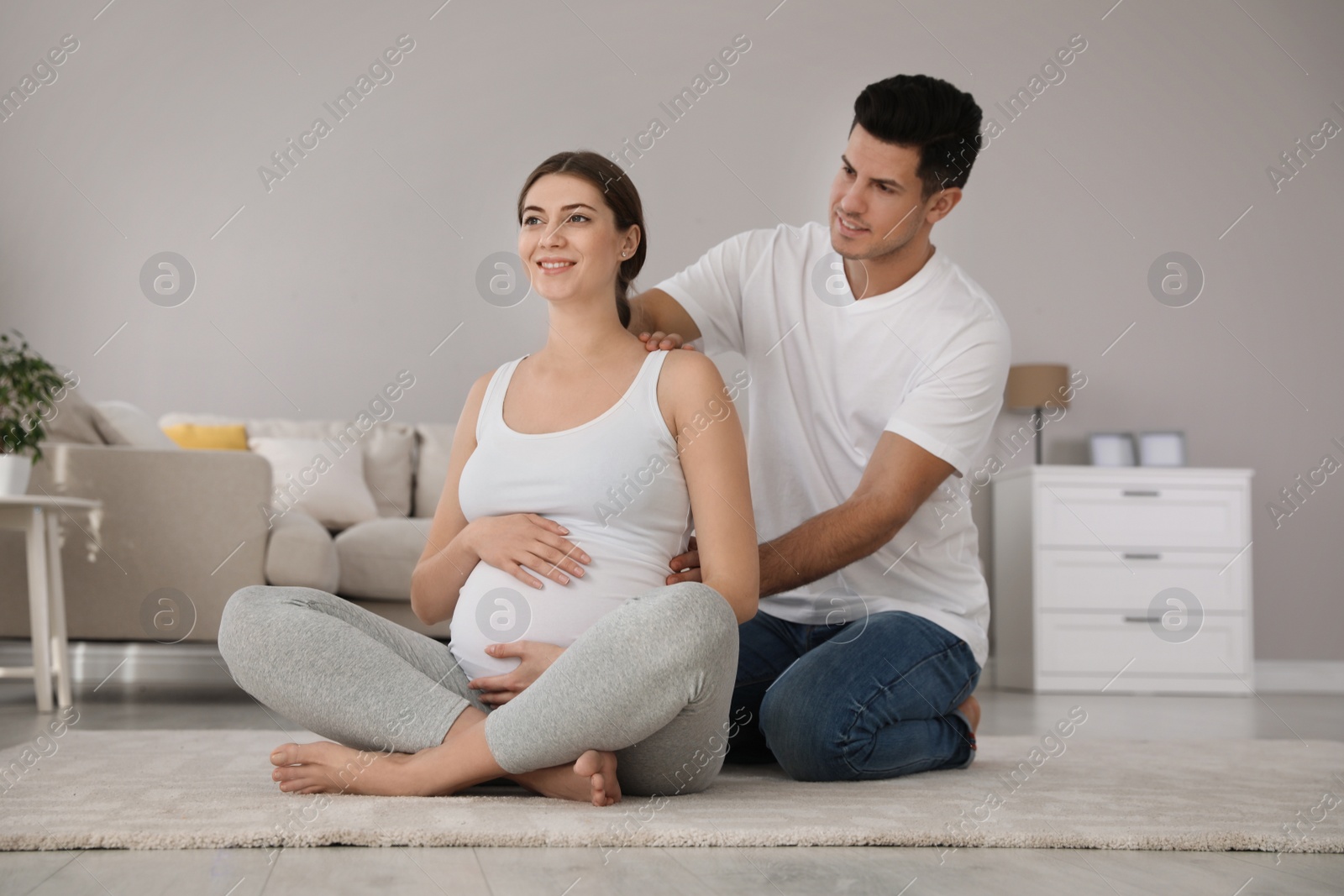 Photo of Husband massaging his pregnant wife in light room. Preparation for child birth