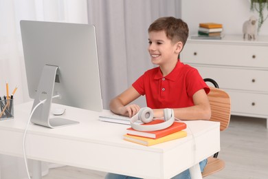 Photo of Boy using computer at desk in room. Home workplace