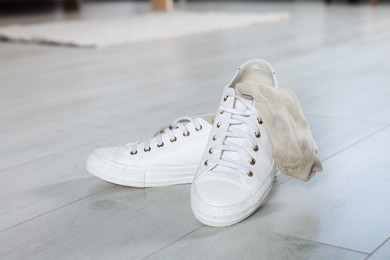 Photo of Sneakers with dirty socks on white wooden floor indoors