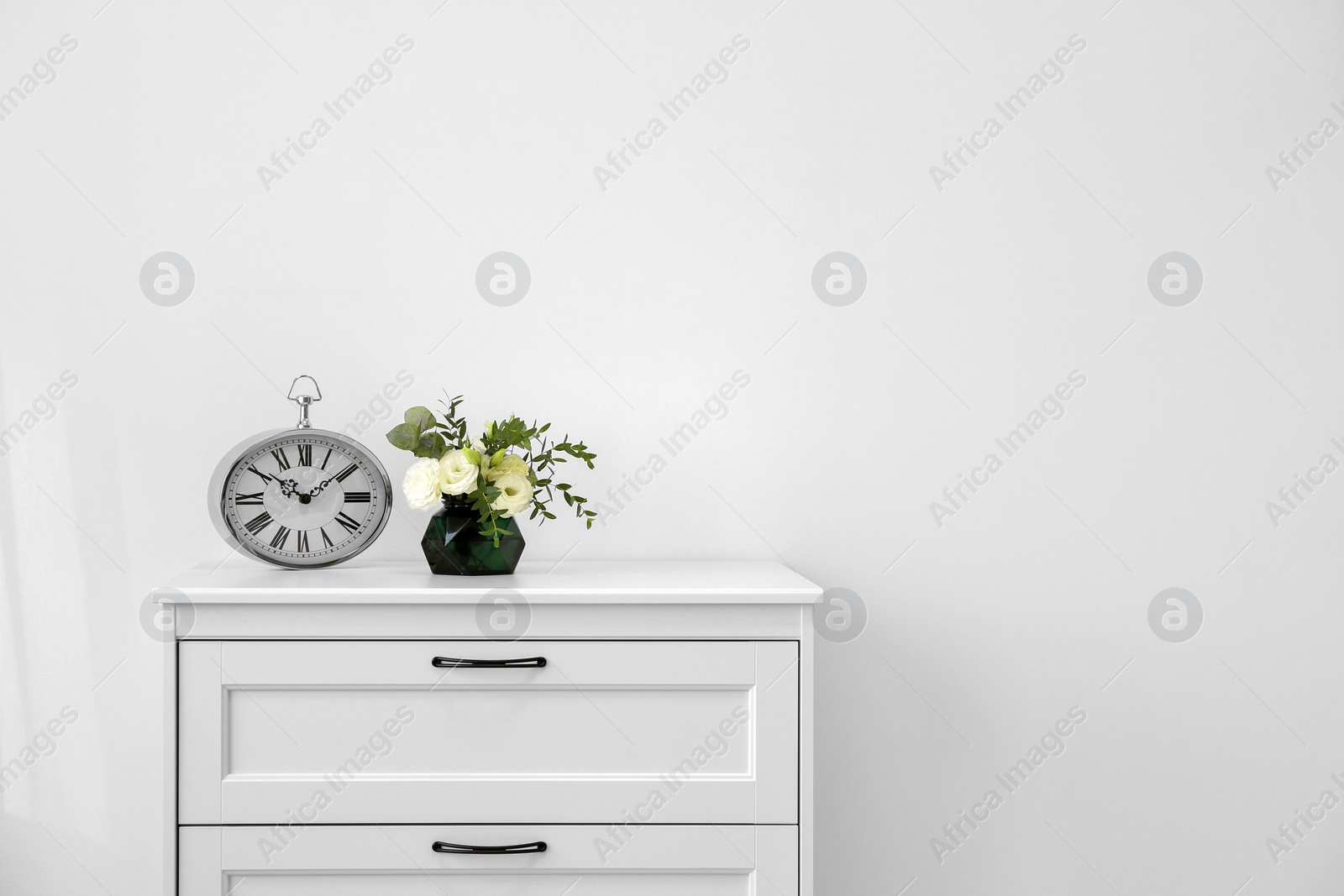 Photo of Modern chest of drawers with fresh flowers and clock near wall. Space for text