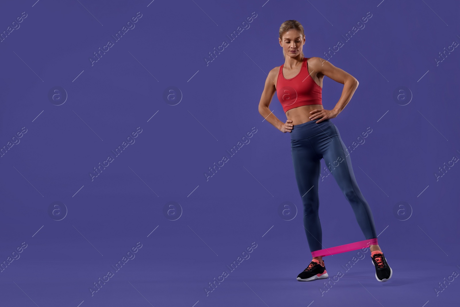 Photo of Athletic woman exercising with elastic resistance band on purple background. Space for text