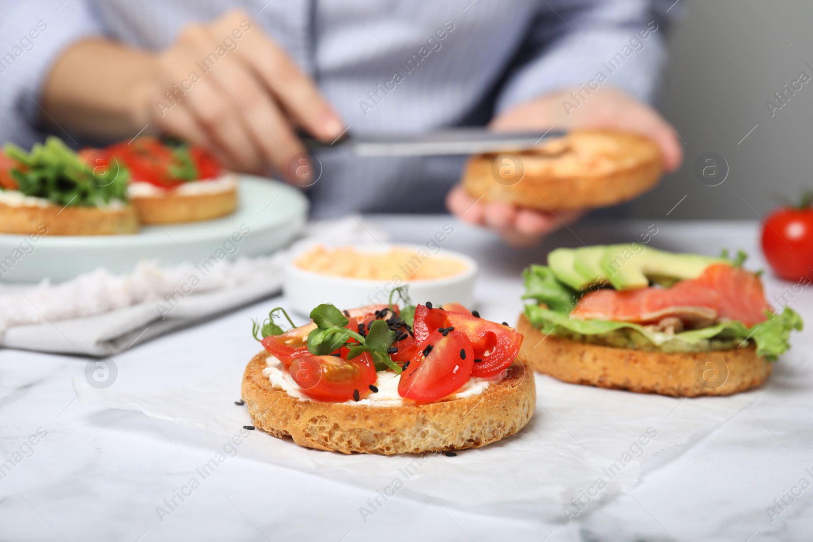 Photo of Woman making tasty rusks with different toppings at white marble table, closeup