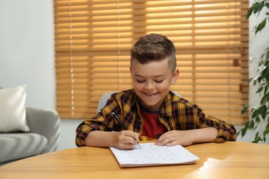 Photo of Little boy solving sudoku puzzle at table indoors