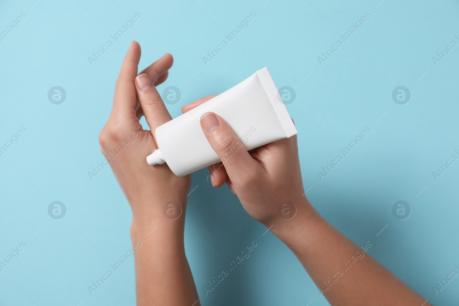 Photo of Woman applying cosmetic cream from tube onto her hand on light blue background, top view