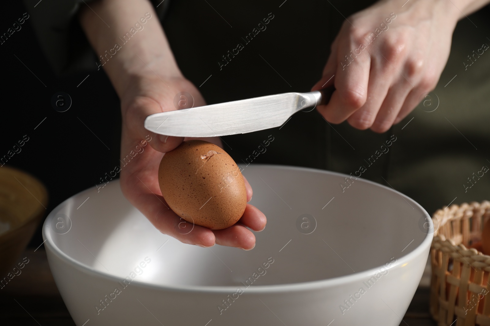 Photo of Making bread. Woman adding egg into dough at wooden table on dark background, closeup