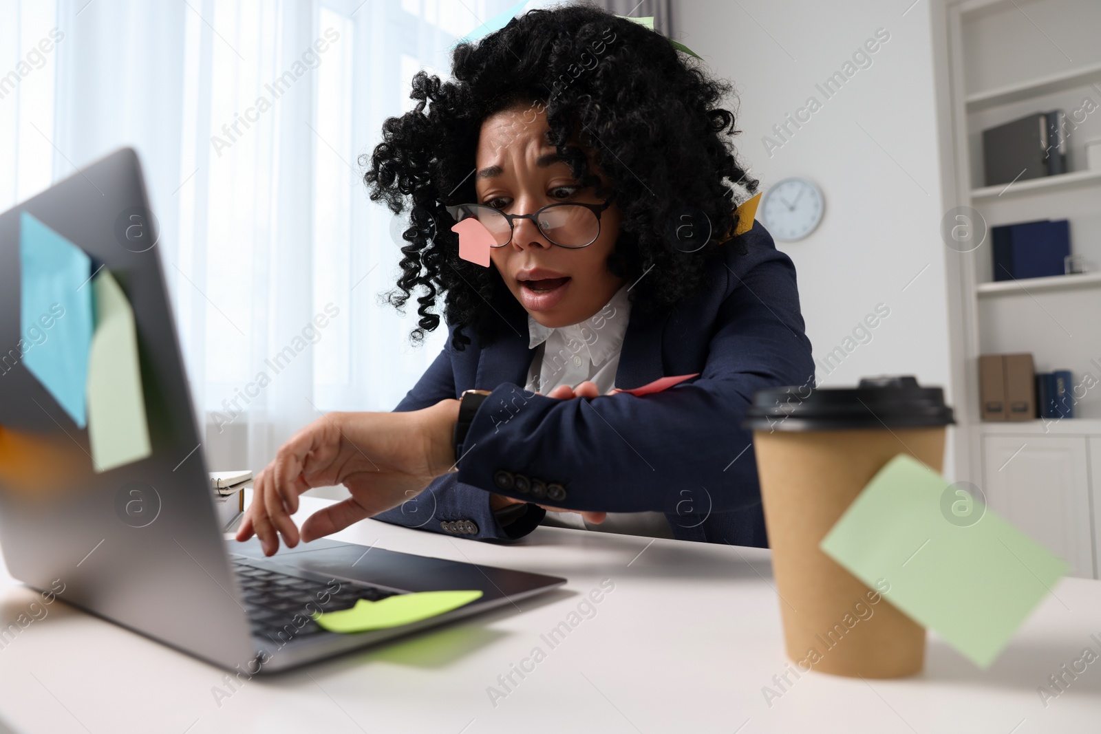 Photo of Deadline concept. Stressed woman checking time near laptop in office. Many sticky notes everywhere as reminders