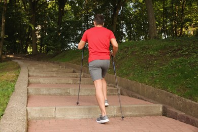 Man practicing Nordic walking with poles on steps outdoors, back view
