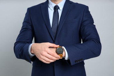 Photo of Businessman wearing wristwatch against grey background, closeup. Time management