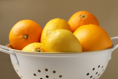 Colander with fresh citrus fruits against beige background, closeup